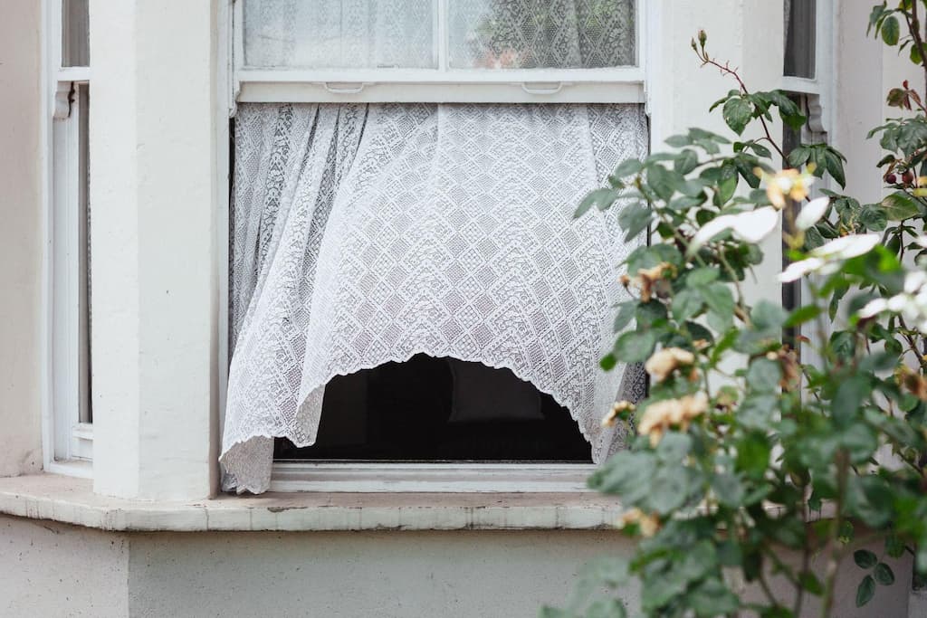 A white lace curtain blowing in the wind through an open window