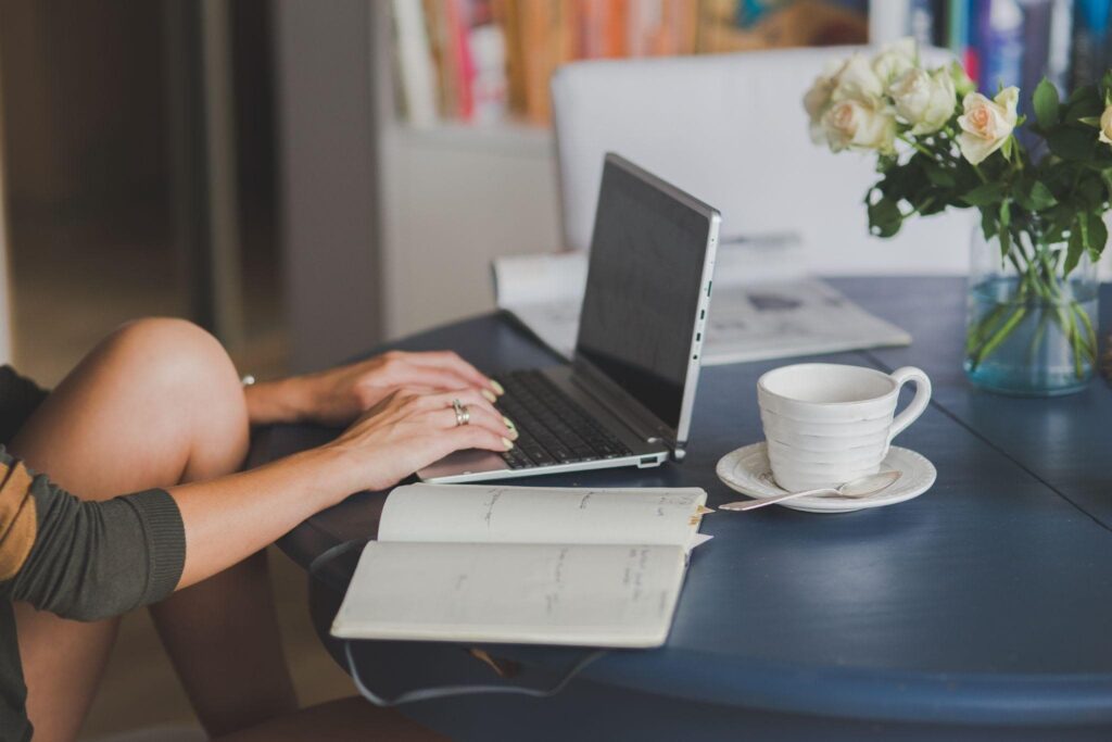 A girl sitting at a laptop with an open notebook and a cup on the table