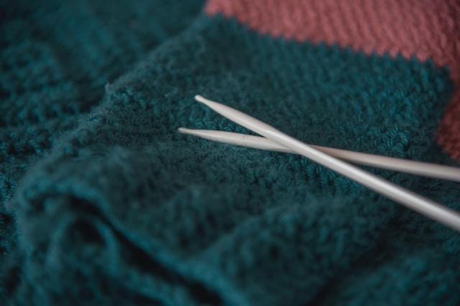 A blue and pink knit sweater and knitting needles on top of it