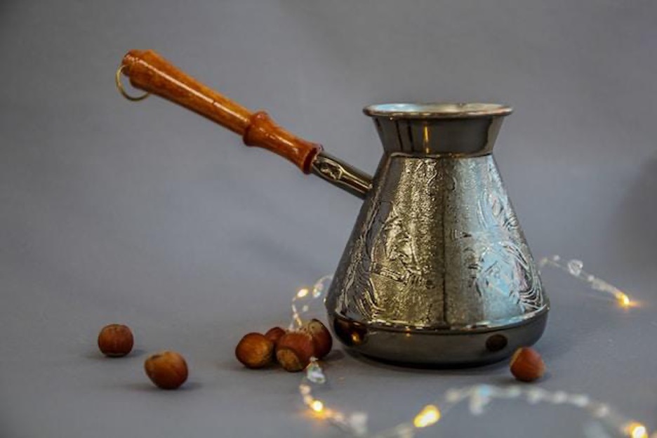 A shiny coffee pot surrounded by hazelnuts