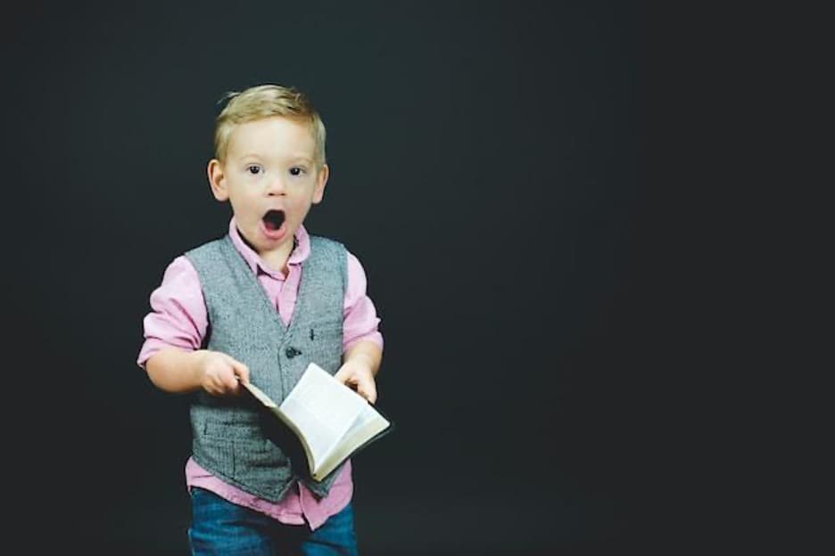 A young boy holding a book, with a surprised face.