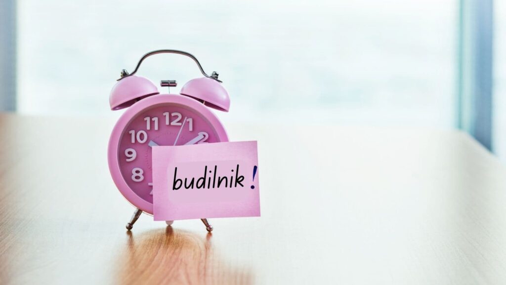 A pink sticky note on an alarm clock with the word budilnik on it