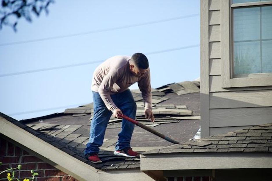 A man standing on top of a half-finished roof, holding a tool.