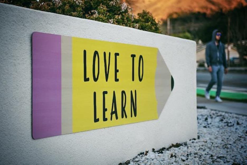 A man walking by a sign with a huge pencil, with the writing “Love to learn"