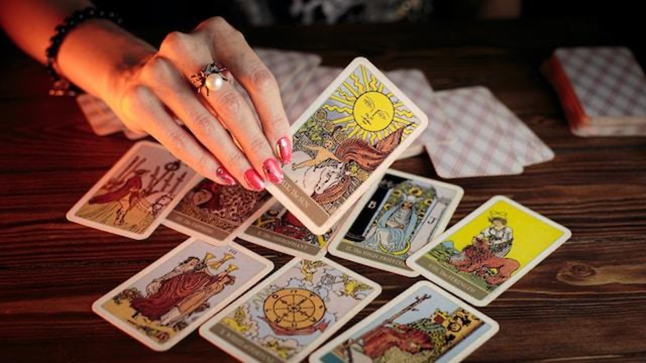 A hand holding a tarot card and a table covered with tarot cards