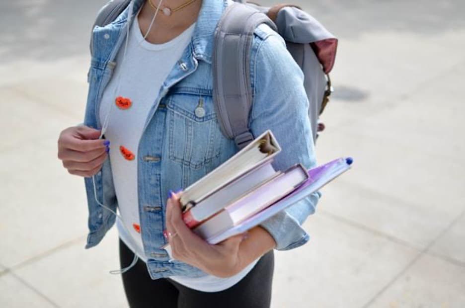 A woman with a backpack on her back holding books in her left hand.