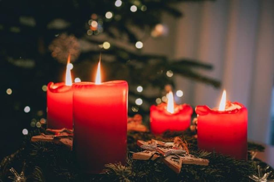 Four lit candles in front of a Christmas tree.