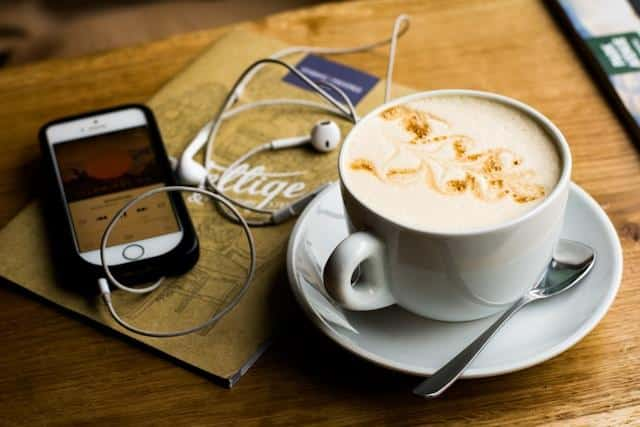 A cup of coffee beside a smartphone with earphones attached.