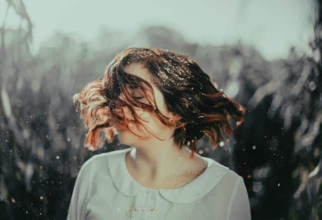A woman wearing a white shirt, shaking her hair and smiling.