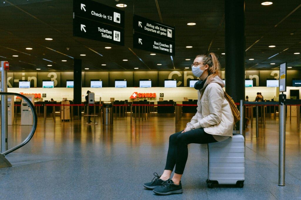 A woman sitting on a suitcase at an airport, or aerodrom — one of the Greek words in Serbian.