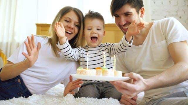 Smiling family celebrating their son's birthday together before blowing candles on a cake.