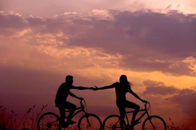 A woman and a man holding hands while riding bicycles as an illustration for Serbian relationship vocabulary.