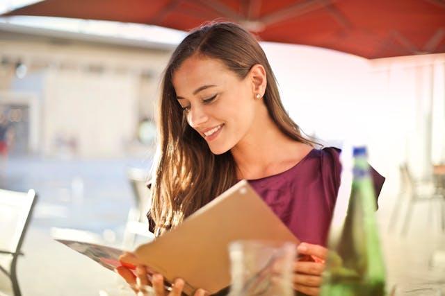 A woman smiling while looking at a menu, planing to order meat in a Serbian restaurant.