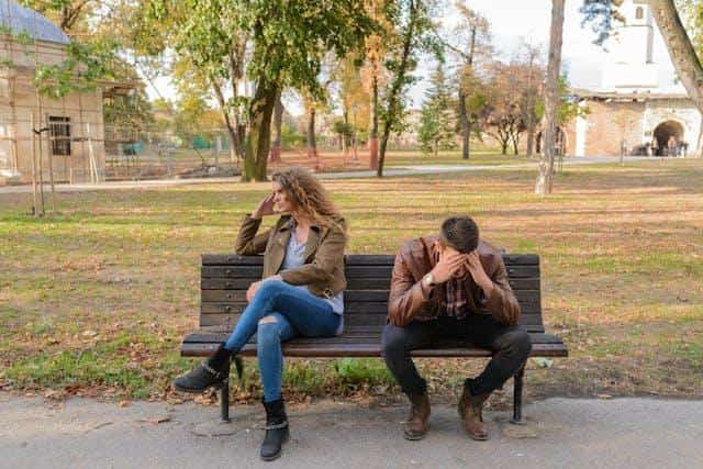 A woman and a man sitting on a bench, looking upset.