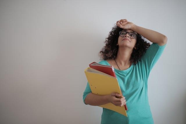 A woman holding folders full of documents, looking overwhelmed.