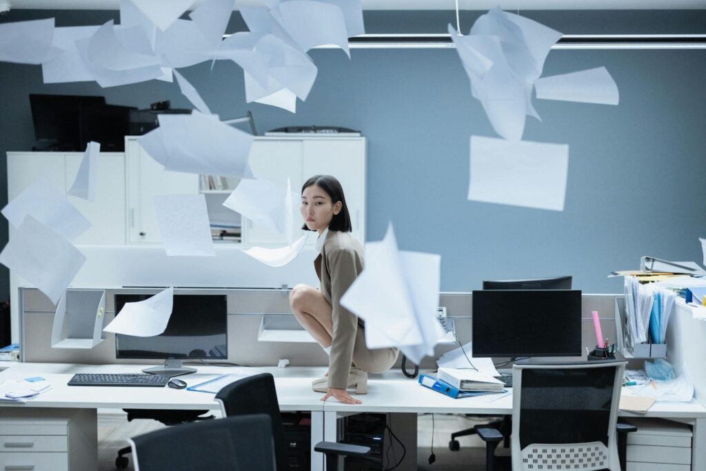 A woman sitting on a desk with papers flying around, overwhelmed by Serbian bureaucracy.