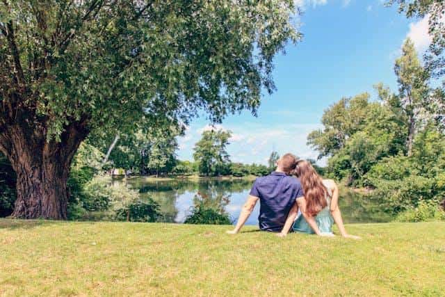 A couple sitting on grass in front of a lake as an illustration of an article about signs you’re dating a Serbian person.