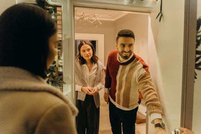 A smiling man and woman opening the door to greet their Serbian neighbors.