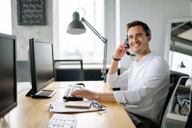 A man in a white shirt sitting in front of a PC, wearing a headset — an illustration of Serbian customer service.