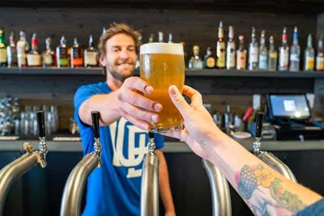 A bartender smiling and handing a beer to a customer.