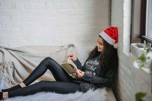 A young woman with a book and a Santa hat resting on the sofa, enjoying one of the public holidays in Serbia.