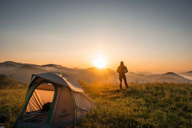 A silhouette of a man standing near a camping tent.