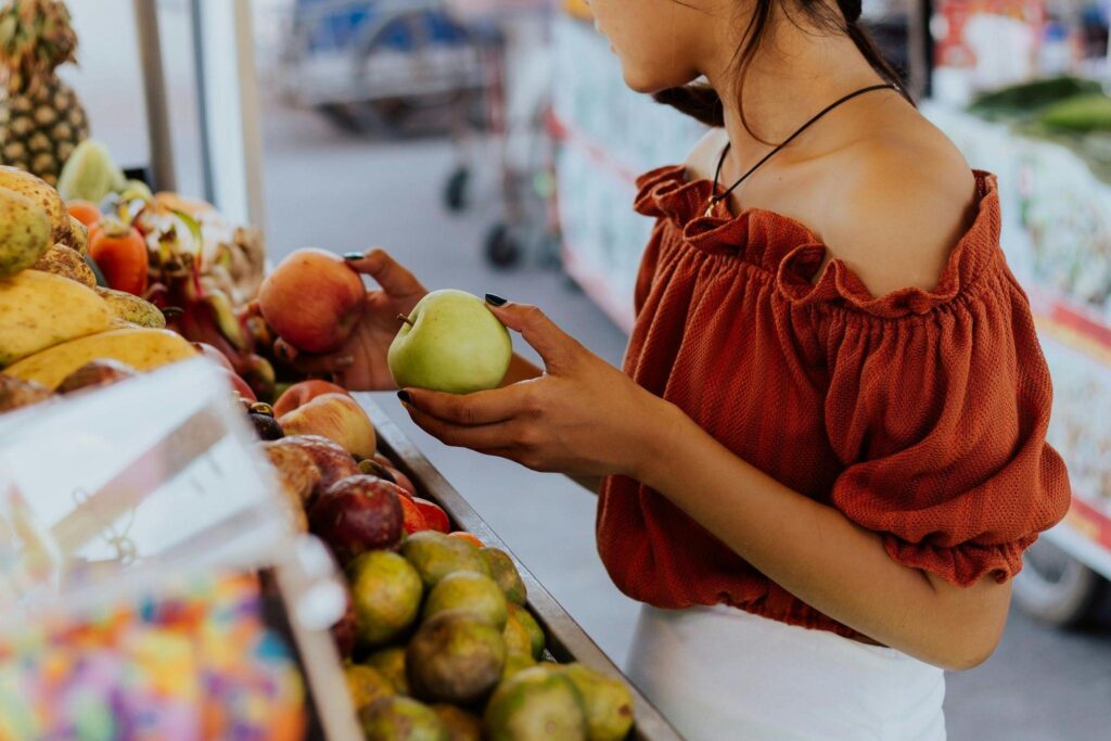 A woman at a market looking at apples — an illustration for Serbian grocery shopping.