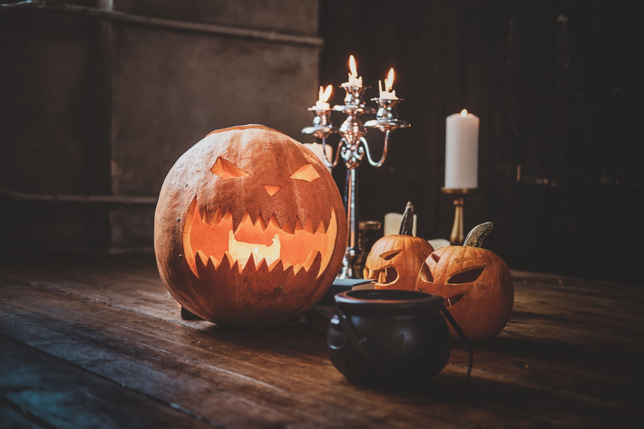 Traditional Halloween carved pumpkins, a small cauldron, and candles on a wooden floor.